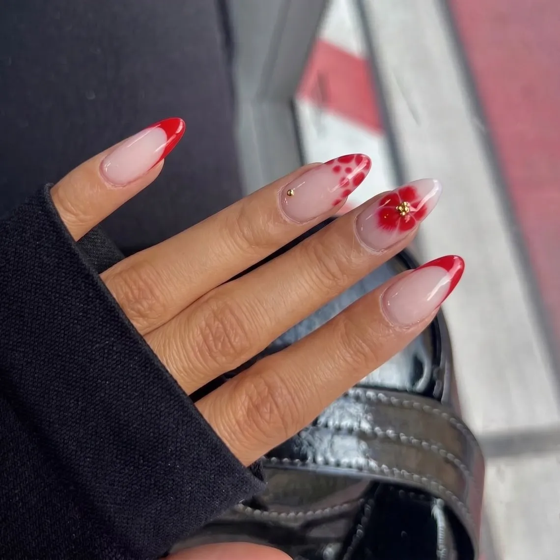Hand mit langen, mandelförmigen Nägeln in roter French-Optik, auf einem Nagel eine gemalte rote Blüte mit kleinen Punkten – das von NAILD generierte Ergebnis